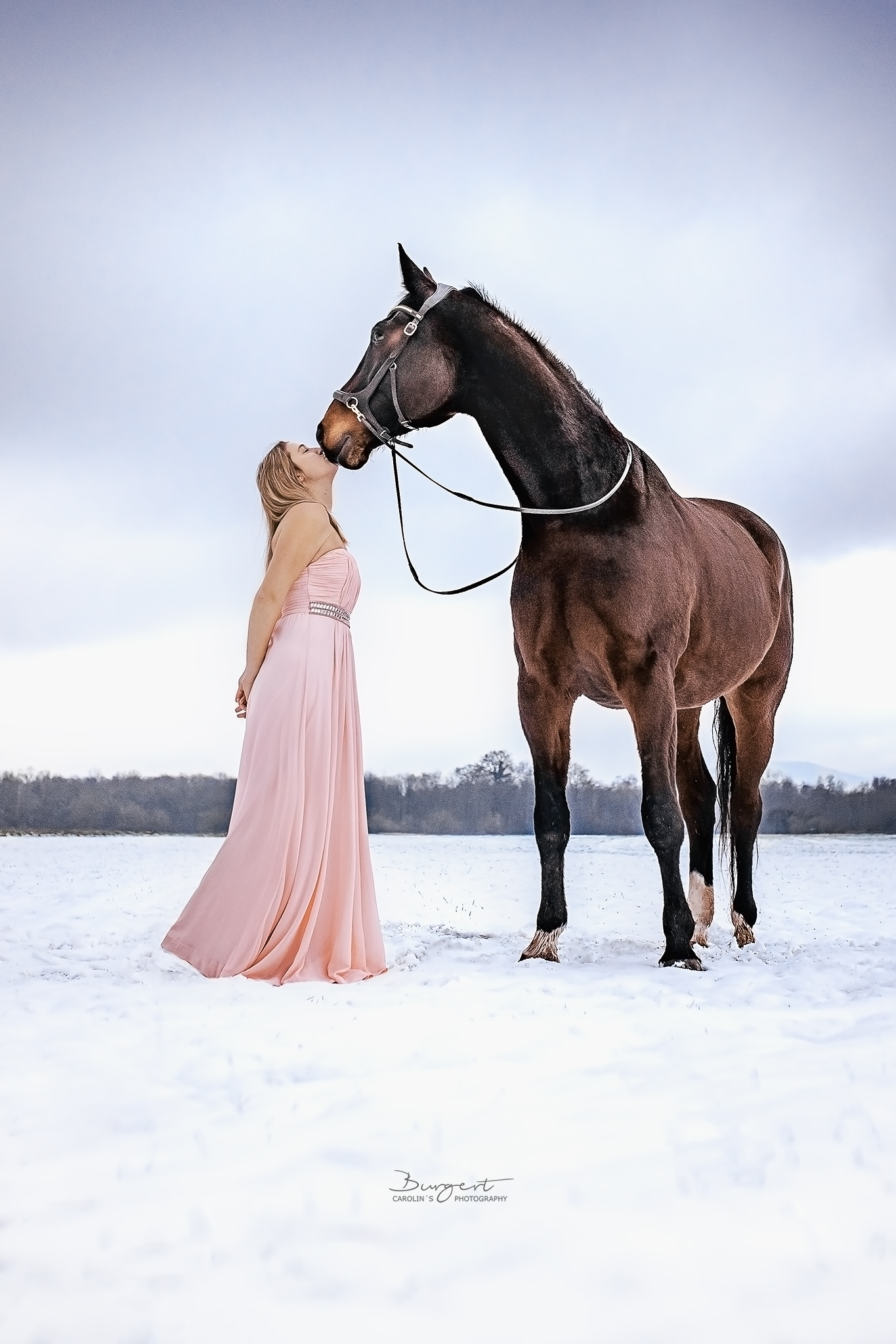 Frau im Kleid mit ihrem Pferd im Schnee